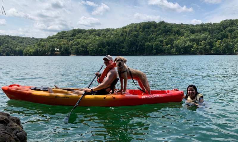 A lake setting. A kayak holds a man with a dog behind him. 