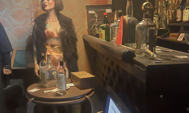 Wax woman dressed as a flapper posing next to a bar with gambling items.