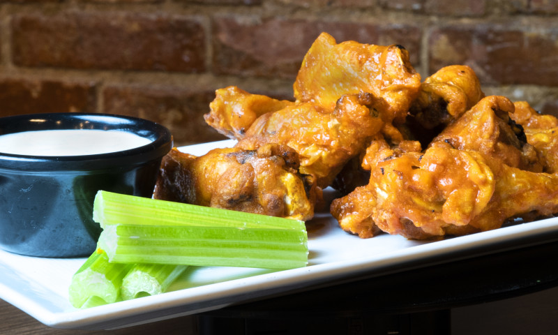 White plate with pile of hot wings and stalks of celery and dip.