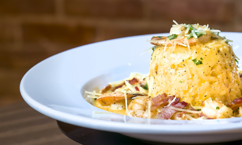 White plate with large mound of creamy grits topped with shrimp, bacon, and scallions.
