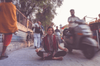 Woman sitting in the middle of the sidewalk with her legs crossed, meditating on the busy street