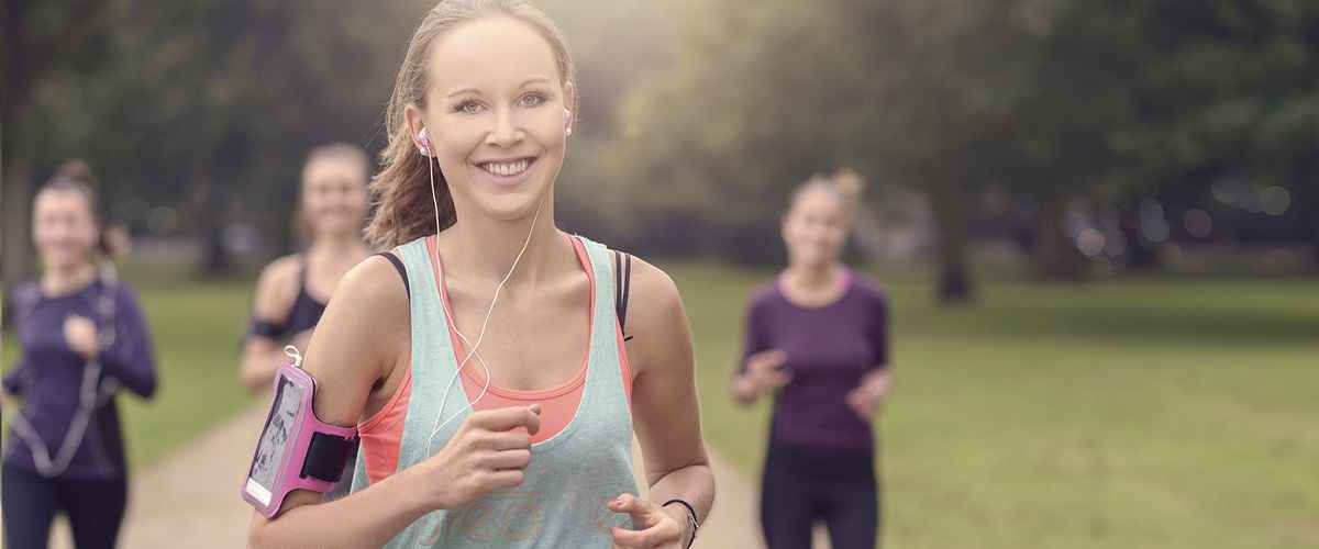 Half Body Shot of an Athletic Pretty Young Woman Smiling at the Camera While Jogging at the Park with Other Girls, with copy space on the right
