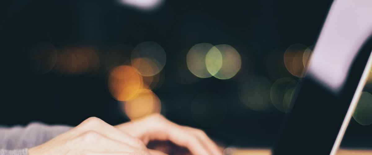Girl hands typing on laptop on wooden table at night