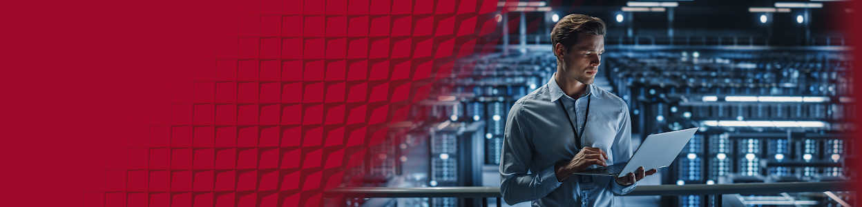 A man in a blue shirt holding a laptop, inside a quantum data center.