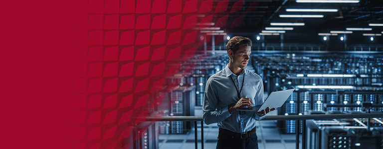 A man in a blue shirt holding a laptop, inside a quantum data center.