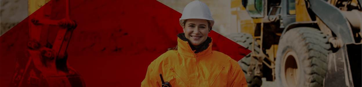 A woman stood with a hard hard and orange workwear jacket on infront of from quarry to construction writing