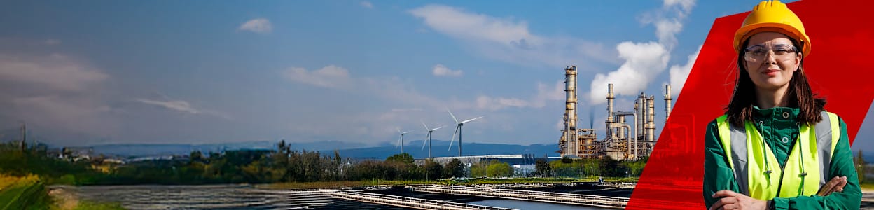 Kvinde iført sikkerhedshjelm og vest, med et kraftværk i baggrunden.