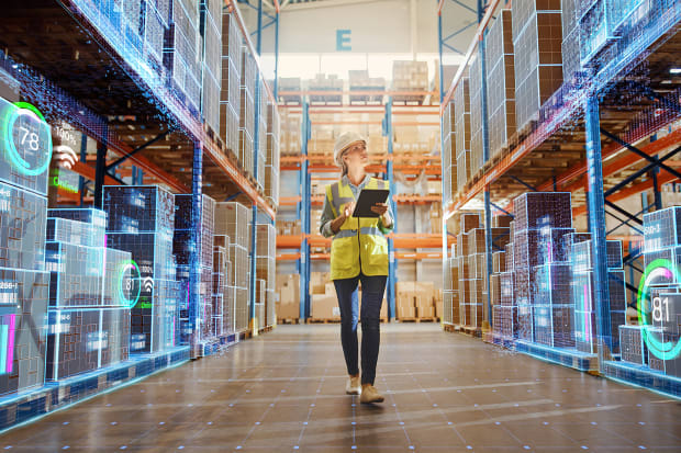 Female wearing high vis jacket and hard hat walking through a warehouse