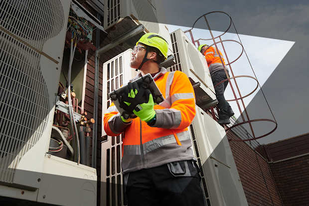 Man in PPE inspecteert installatie met tablet in de hand