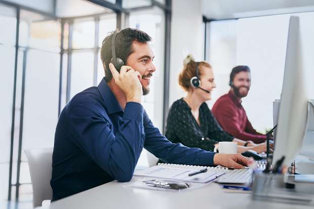 Image of a call centre with 2 men and one woman in front of computers on the phone with headsets on