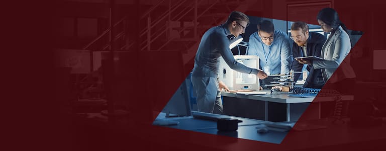 Eine Gruppe von Ingenieuren, die über einen Tisch in einer Design-Werkstatt gebeugt ist.