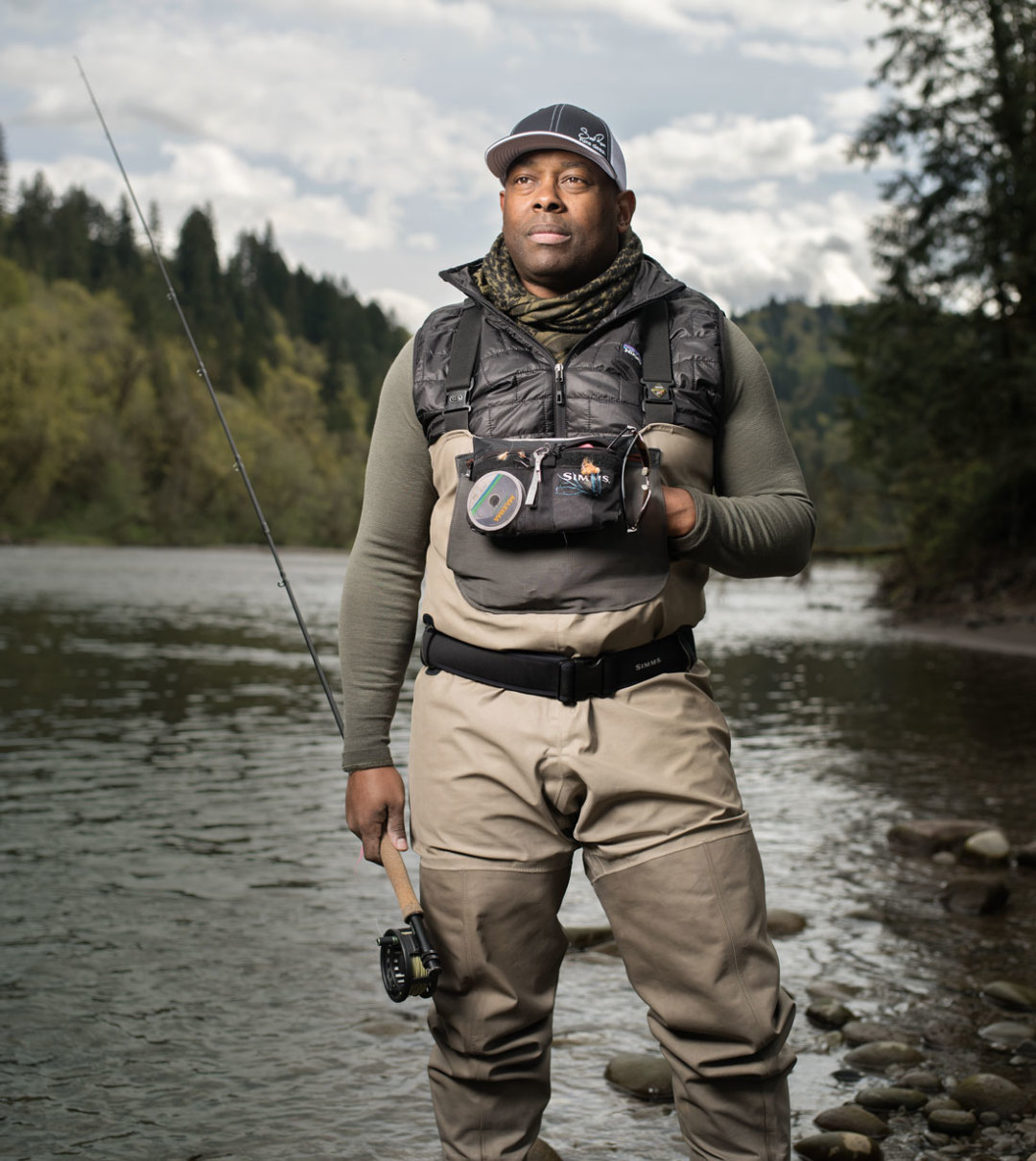 A woman in waders stands in a rushing river with a fly fishing rod