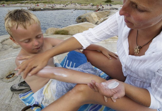 Kvinne smører solkrem på gutt 7 år. Sommer, bading og soling. Mor og barn.