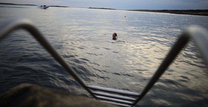 Kvinne bader mens fritidsbåt kjører i bakgrunnen. Mærrapanna, Fredrikstad kommune, Østfold. NB: Modellklarert. Foto: © Thorfinn Bekkelund / Samfoto