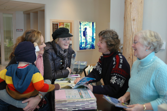Volunteers Sherry Freels (second from right) and Sally Bell (far right) offer advice to a visiting family at the Traverse City Visitor Center.