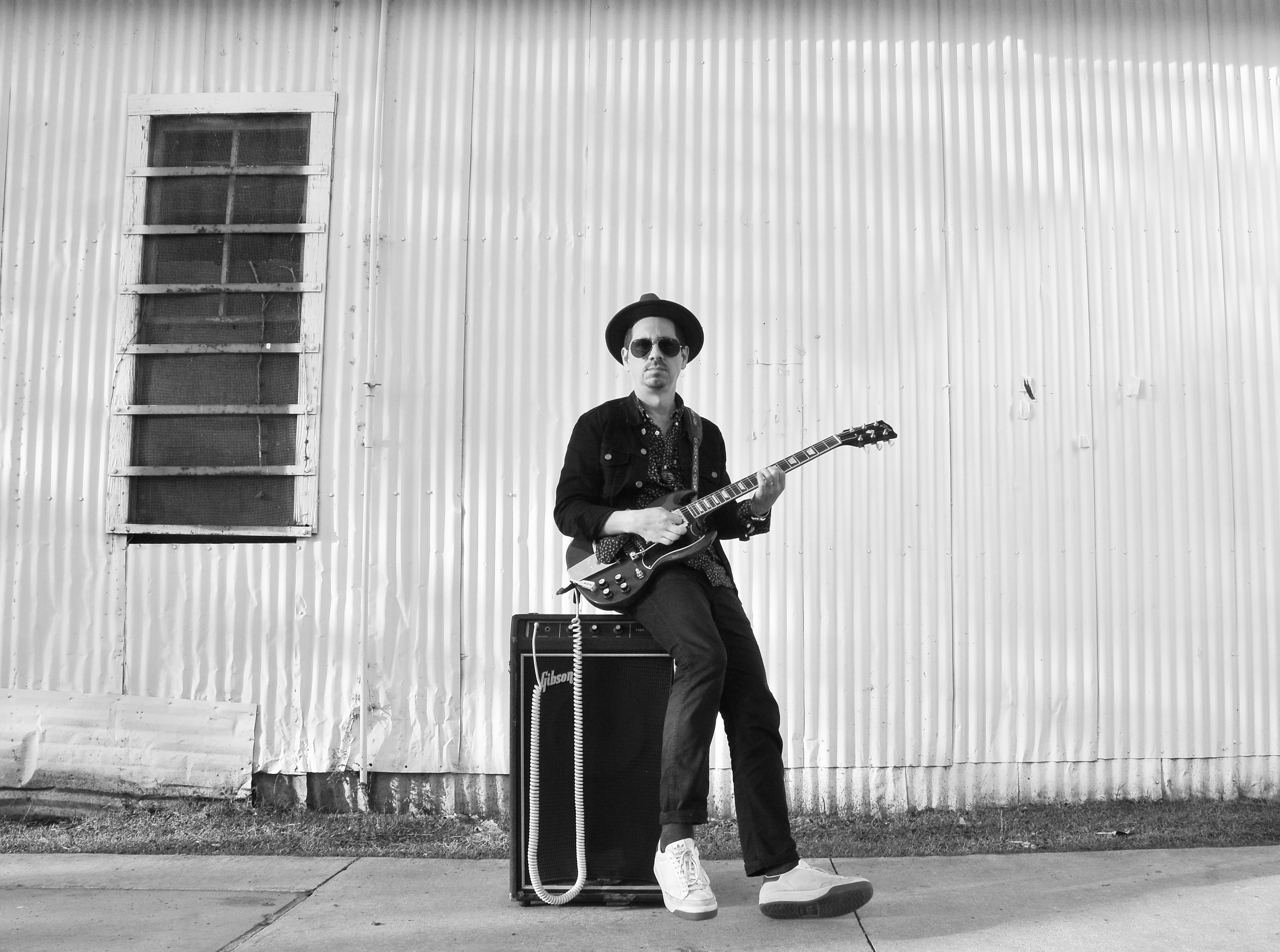 Adrian Quesada portrait with guitar sitting on amp