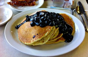 Blueberry Pancakes with lots of blueberries and syrup and a side of bacon.