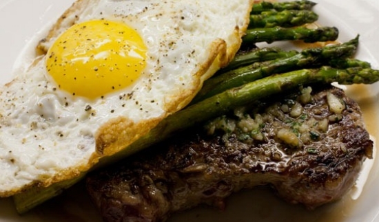 A fried egg atop steak and asparagus