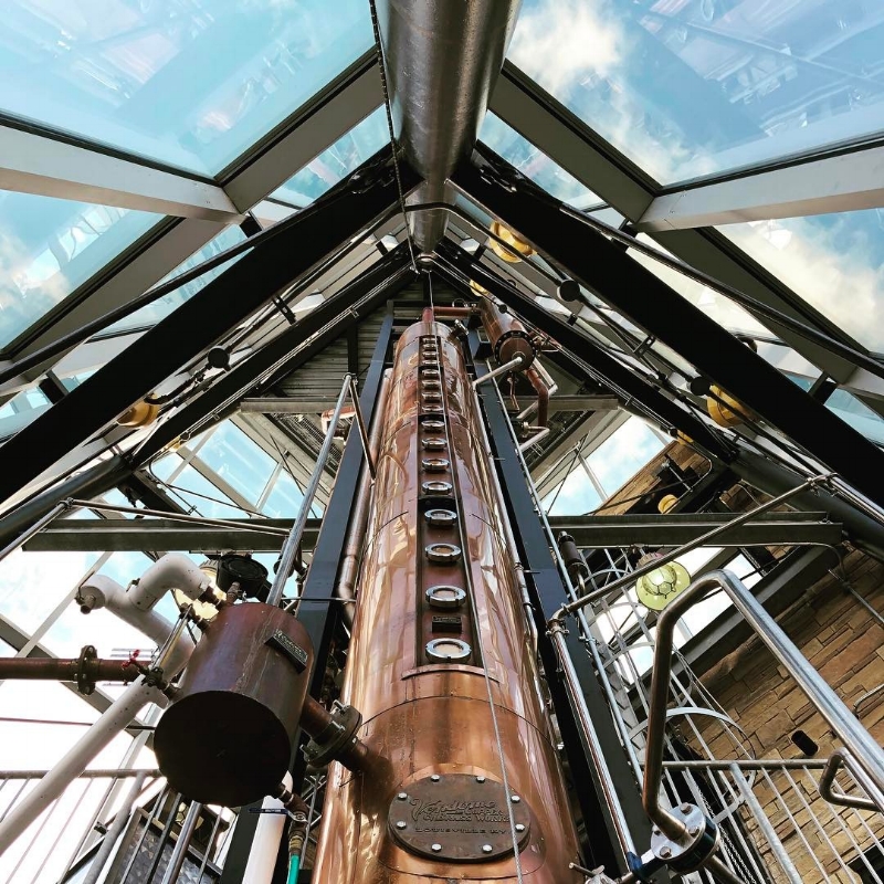 A copper column still that's three stories high, surrounded by clear windows.