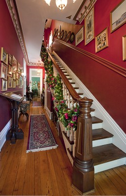 Beautiful 19th century staircase with hardwood floors and Christmas decorations and a red wall.