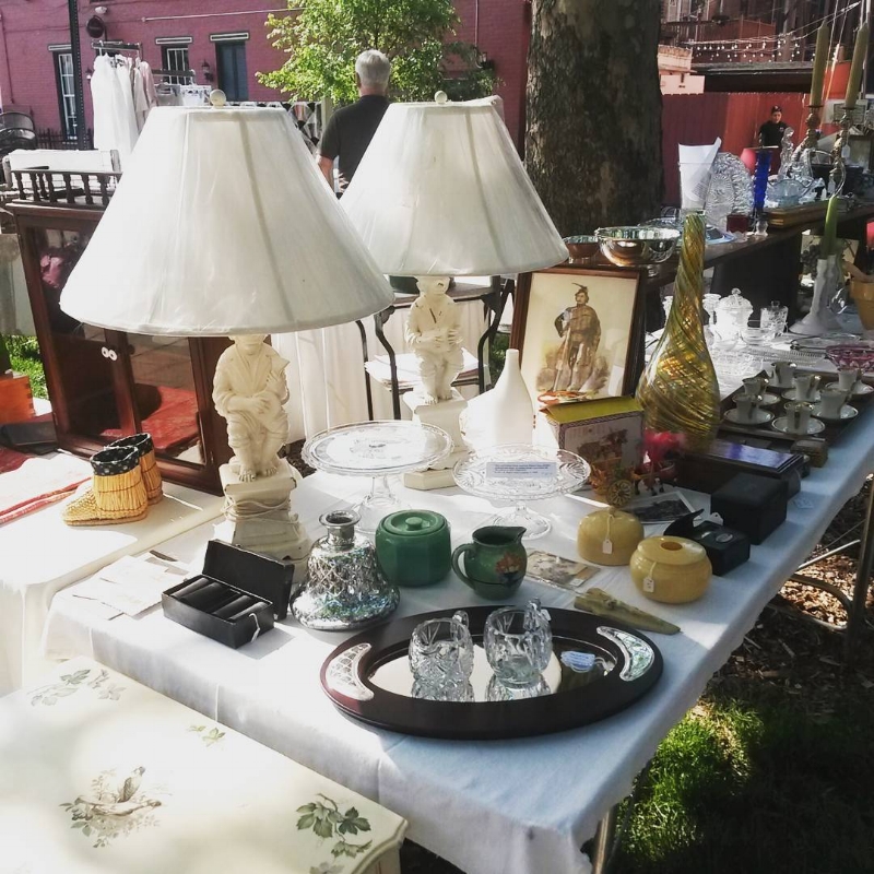 Long table with white cloth outside at Mainstrasse Village, covered in lamps, ceramics and collectibles