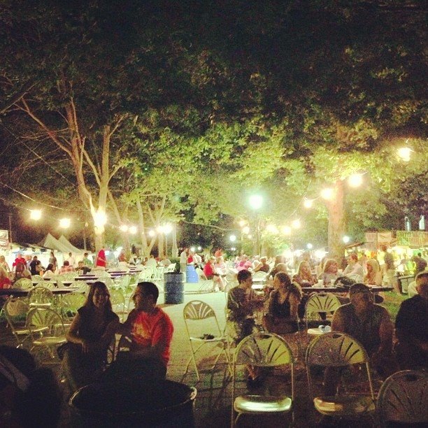 families seated on the grass under strings of white lanterns at goetta fest in Mainstrasse Village