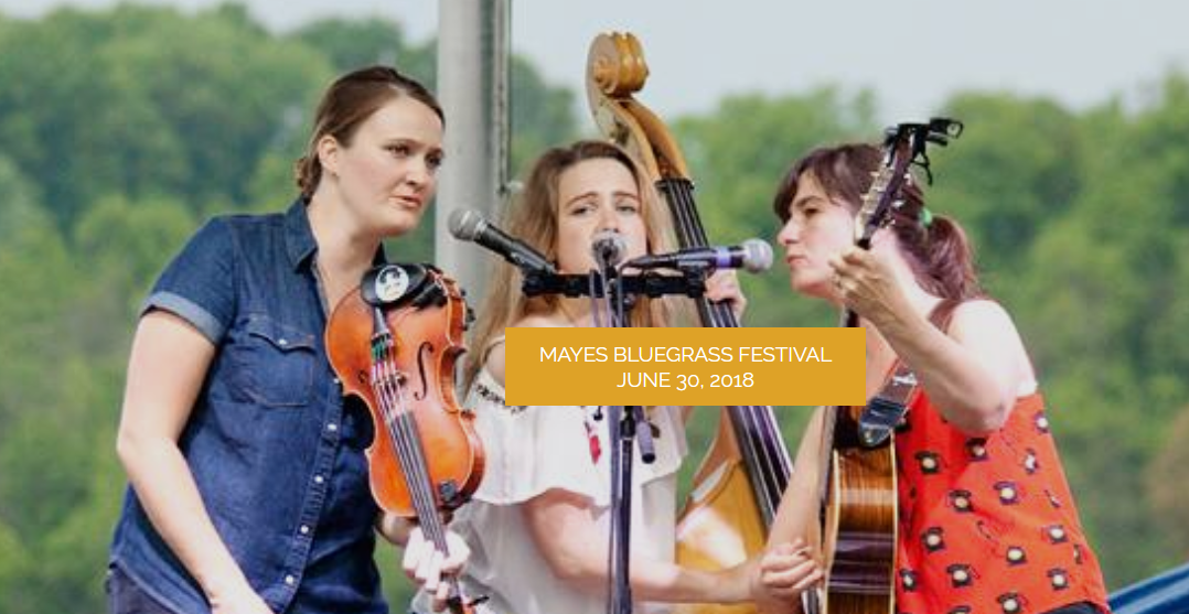 Three women gathered around a microphone singing and playing bluegrass music