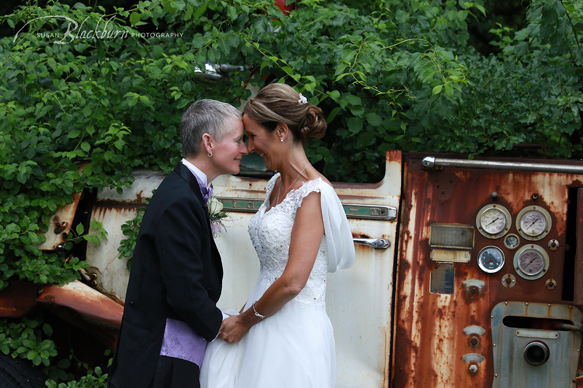 Couple holding hands and smiling after wedding in front of trees and vintage truck