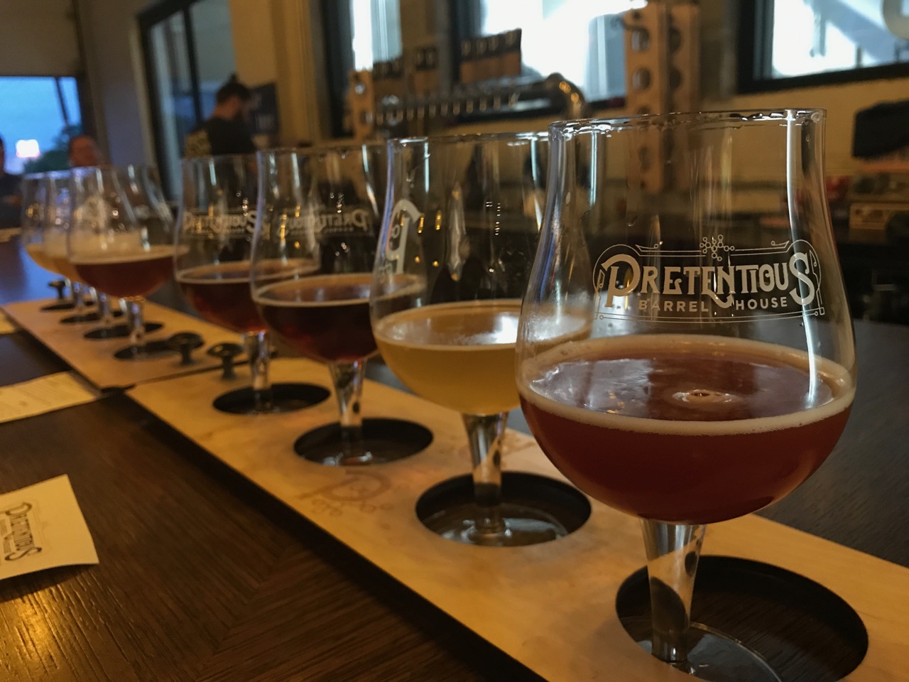 Two flights of four different beers in glasses labelled with Pretentious Brewing's logo