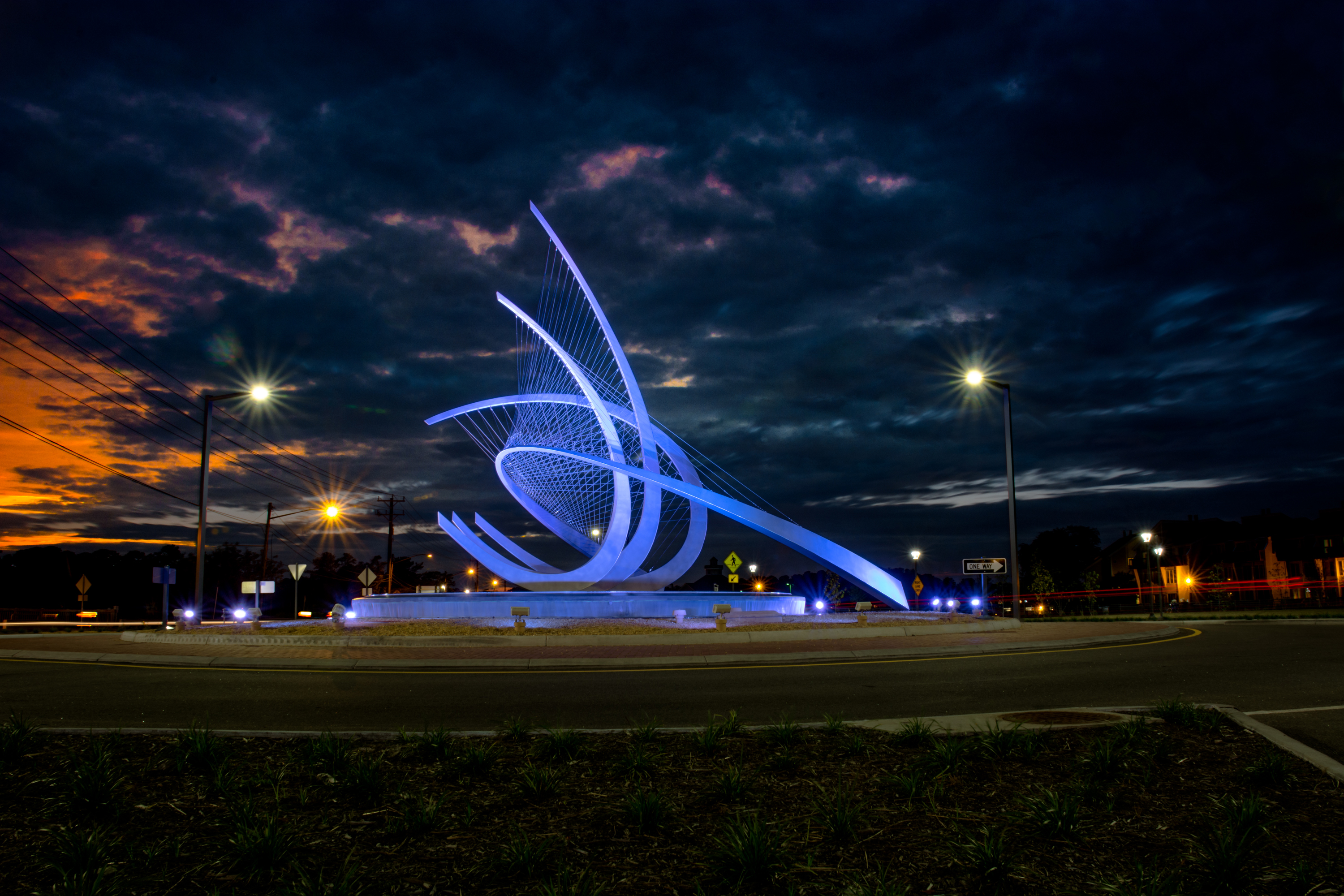 After a national search, the Public Art Virginia Beach Foundation, along with professionals from Virginia MOCA and the Chrysler Museum of Art, selected Jeff Laramore's piece entitled, Wave, a 35-foot stainless steel sculpture, to grace the entry to the Laskin Gateway. It rests in a 35-foot wide reflecting pool inside the Laskin Road Roundabout. "Wave" has an open design that will allow high winds to pass through reducing resistance. To ensure longevity, the sculpture was fabricated out of a combination of marine grade stainless steel plates and stainless steel cables. And, the sculpture will be enhanced with a colorful display of programmed lighting for visibility in the evening.The new sculpture was dedicated on Oct. 12, 2013 and provides a strong and beautiful sense of arrival to a very special destination. Founded in 2012, the first initiative of the Foundation has been to raise funds to commission this piece for the new Gateway to Laskin Road and its continuing goal is to showcase Virginia Beach as a welcoming and creative city that takes great pride in its public spaces.Watching all the pieces come together was an amazing process. If you get a chance take a walk around the Wave and see all the angles at night. It's simply stunning.