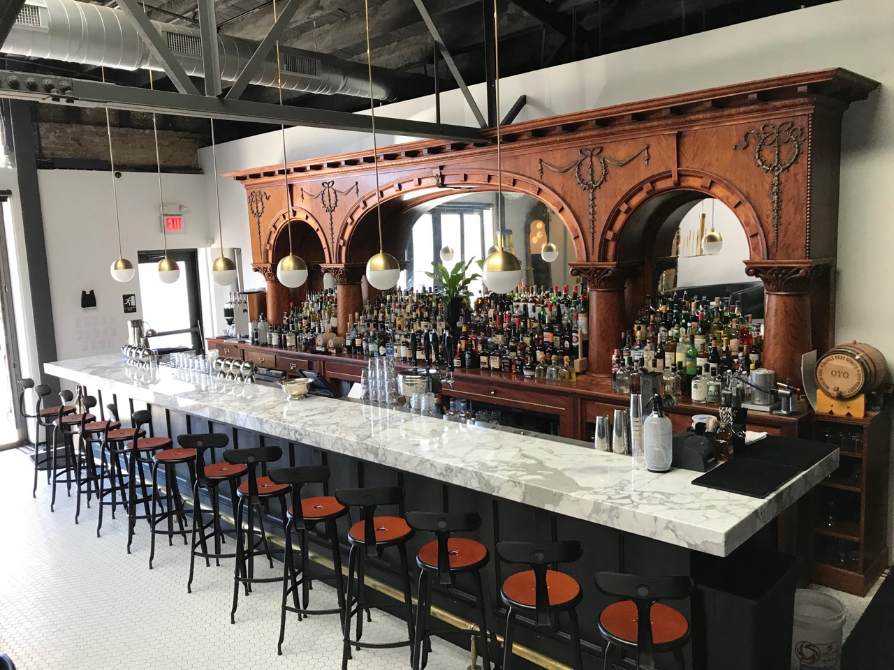 Interior view of Service Bar, featuring white marble bar, wooden stools, hanging lights, and antique wooden shelving fully stocked with bottles