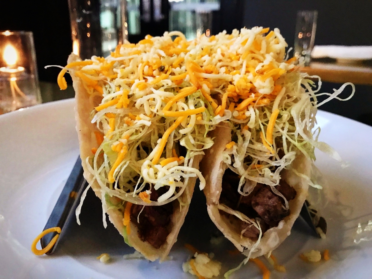 Two Cheesy Brisket Crunch tacos on plate at Service Bar, piled high with meat and cheese