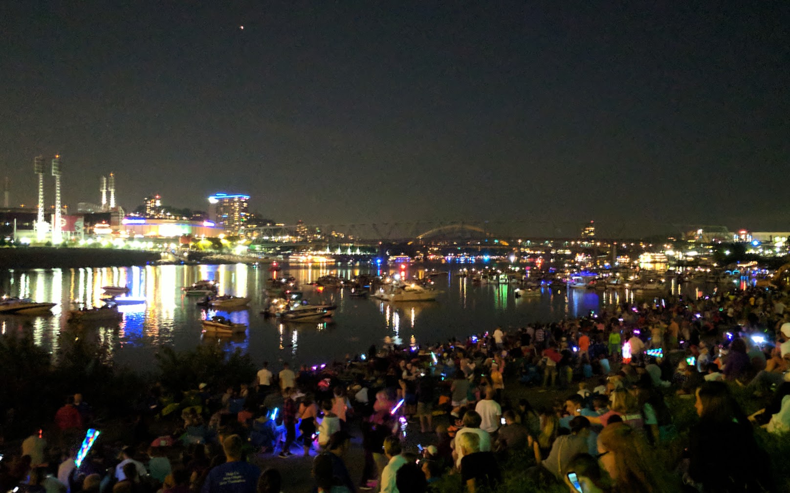 A crowd of people in the dark, sitting on the banks of the Ohio river at Riverfest
