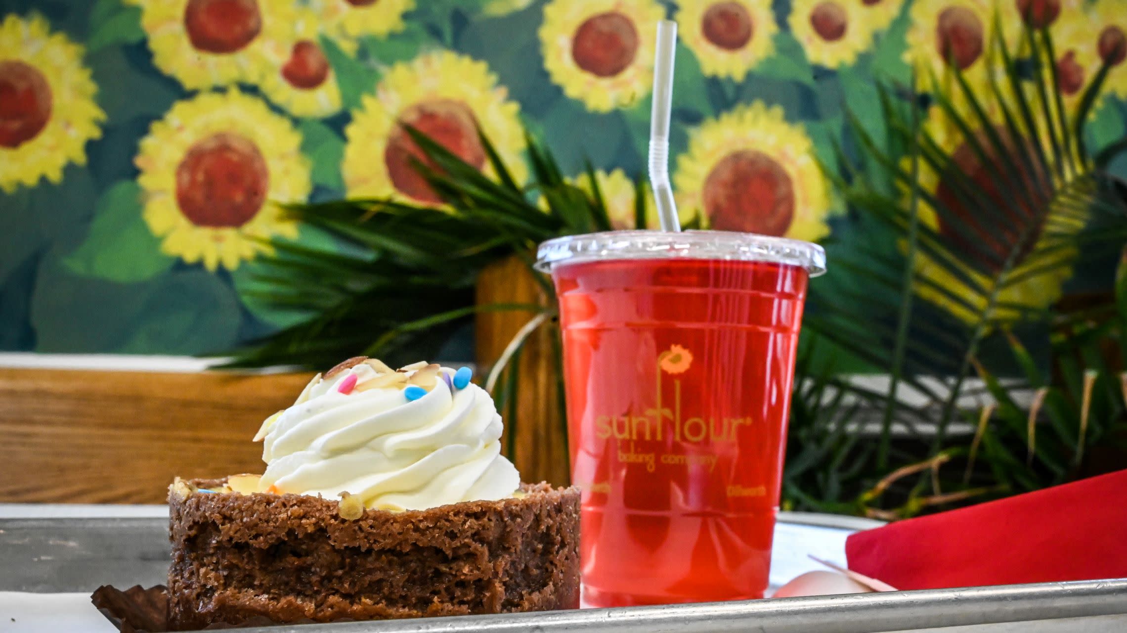 drink and dessert on table alongside wall painted with sunflowers