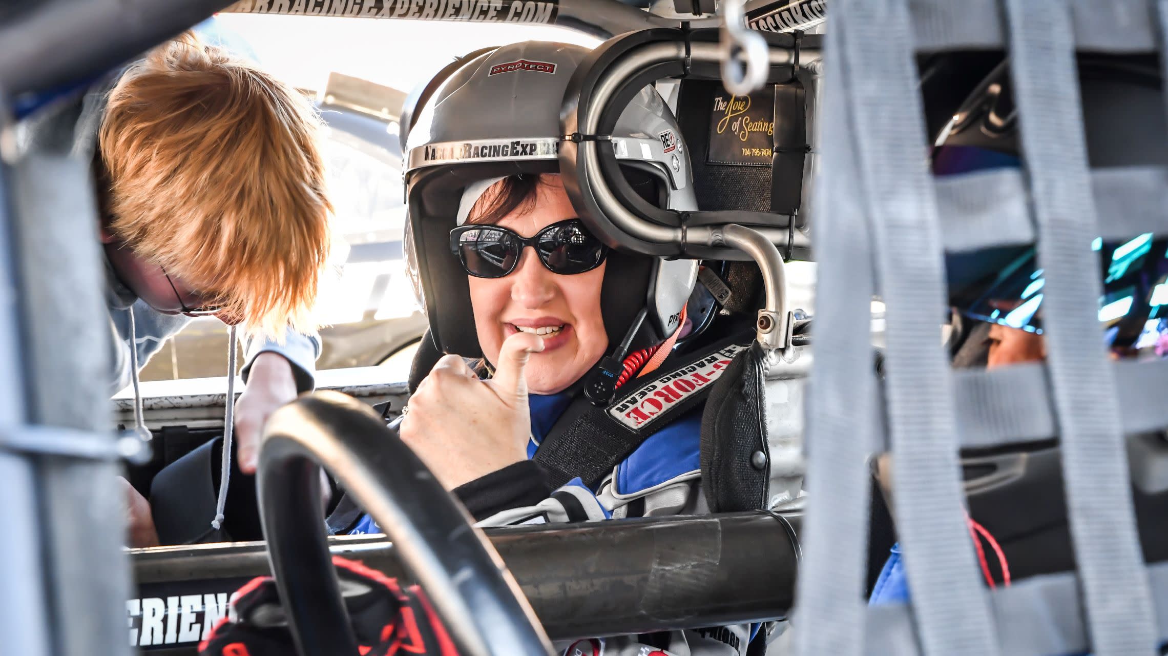 woman gives thumbs up from inside race car