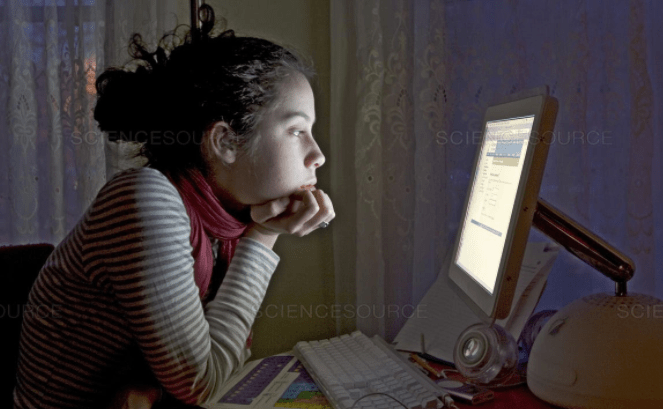 A teen girl sits at a computer. 