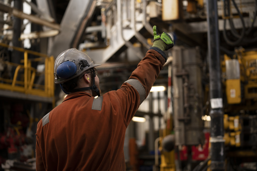 One technician wearing safety gear works on industrial machinery.