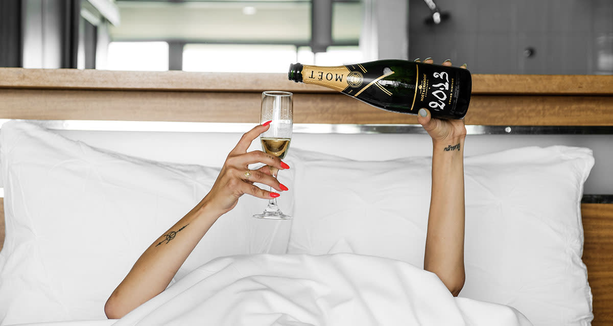 Hands holding champagne glass and champagne bottle while tucked under the sheets in bed