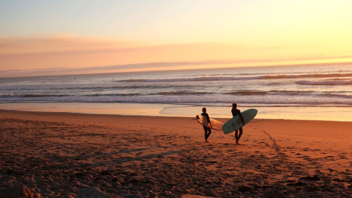 Two people on the beach carrying surfboards at sunset