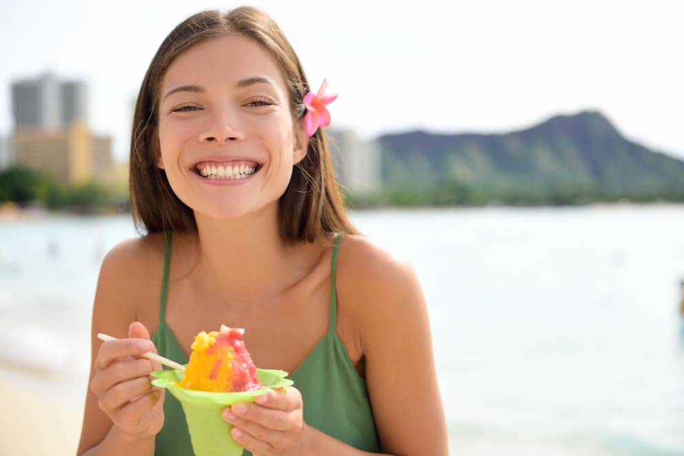 woman eats shave ice on waikiki beach overlooking diamond head