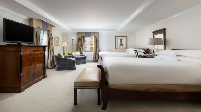 This photo showcases our 450 - 500 square foot room, featuring either two King size or two Queen size beds against the side wall separated by an elegant table with a table lamp, phone and alarm clock. A sitting bench is also situated at the foot of the bed. Located near the window there are two comfortable armchair with an additional side table and standing lamp. The room also features an armoire, 37 inch flat screen TV and a full stocked mini bar. The bathroom is made with Italian marble and features a 55 gallon soaking tub.