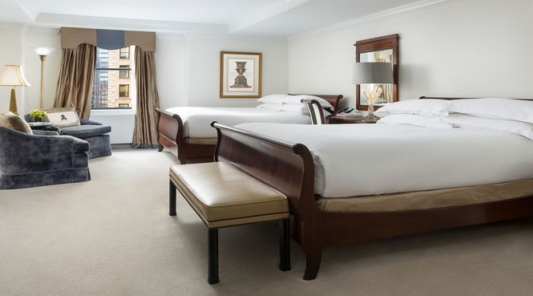 This photo showcases our 495 square foot room, featuring two Queen size bed against the side wall with one night stand between the two beds. Across from the beds there is a seating arrangement which consists of two armchairs and a small table. In addition there is an armoire with dresser drawers and a 43 inch flat screen TV. Next to the armoire you will find a fully stocked mini bar, including wine, bottled beverages and assorted snacks available for purchase. The room also features a full size work desk, an Italian marble bathroom with a 55 gallon soaking tub and a vanity.