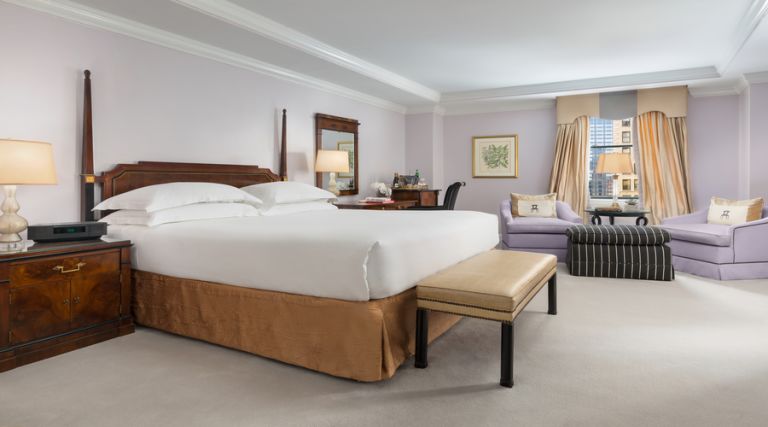 This photo showcases our 450 - 500 square foot room, featuring one King size bed against the side wall with two night stands on each side with a phone and a alarm clock, and sitting bench at the foot of the bed. Across from the bed there is an armoire with dresser drawers and a 43 inch flat screen TV. Next to the armoire you will find a fully stocked mini bar, including wine, bottled beverages and assorted snacks available for purchase. Located near the window there are two comfortable armchairs with an ottoman and side table. The room also features a full size work desk, an Italian marble bathroom with a 55 gallon soaking tub. Wall decor includes a wall mirror and Italian inspired artwork.