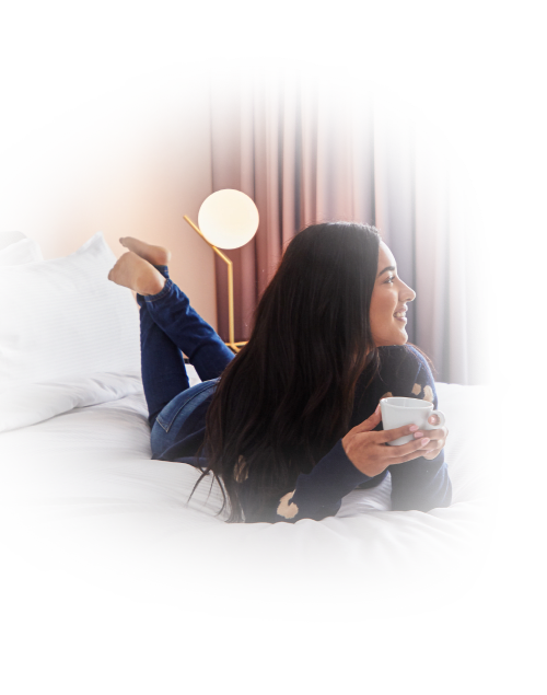 Women holding a coffee cup lying on the bed and looking sideways