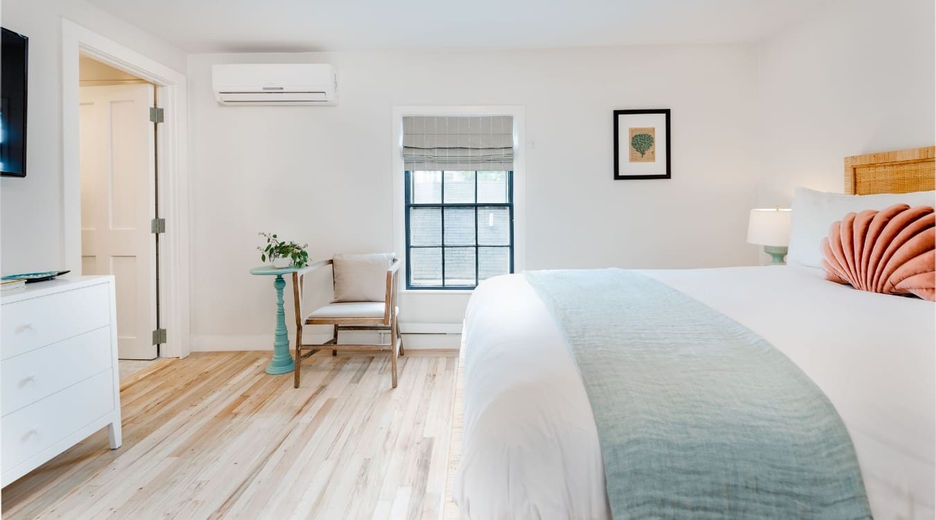 To the left we have a chair with table. AC and TV are fixed to wall. To the right there is a painting fixed to the wall and a table lamp is placed beside the bed.
