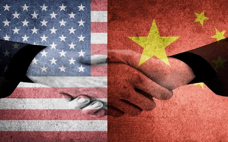 A pair of hands shaking over an American and Chinese flag in unity.