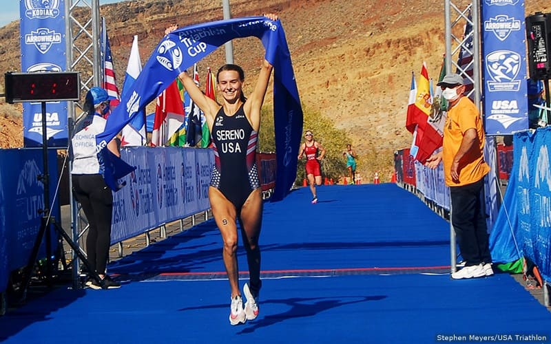 triathlete gina sereno crosses the finish line first, holding the race tape banner at the americas triathlon championship in st. george utah