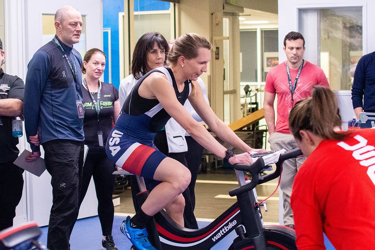 Coaches watch a power meter as an athlete rides an indoor bike trainer.