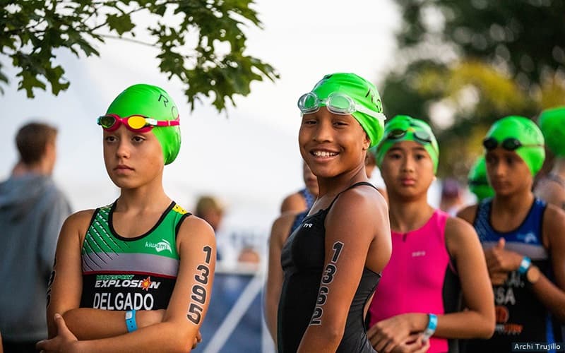 Photo of youth triathletes smiling. They are wearing green swimcaps and trisuts.