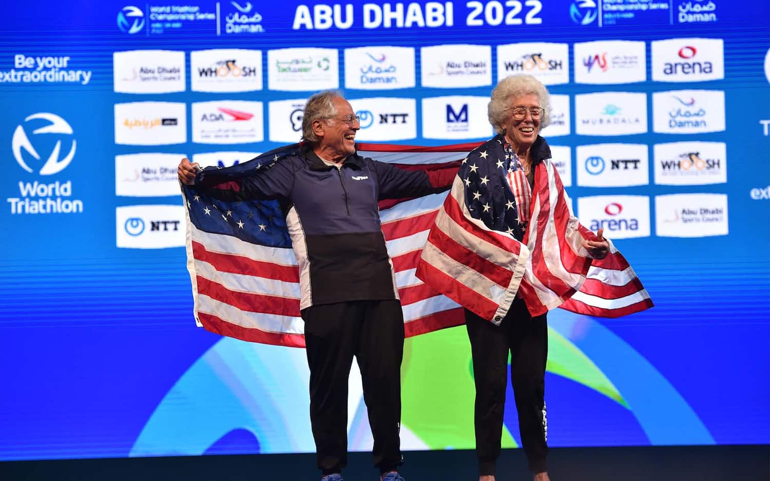 two age group athletes hold up the US flag on the podium in Abu Dhabi